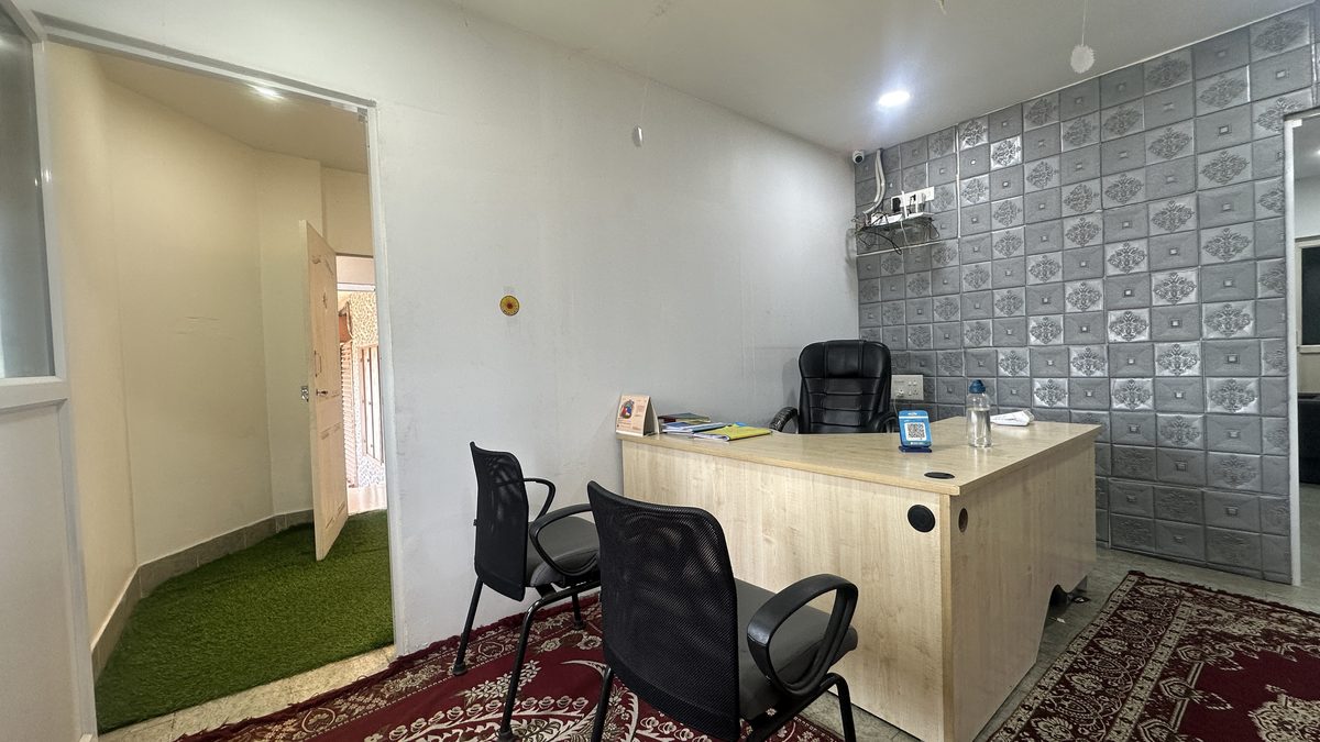 The reception: a wooden desk with a card machine on it, two chairs facing it for visitors, and a patterned grey feature wall behind.