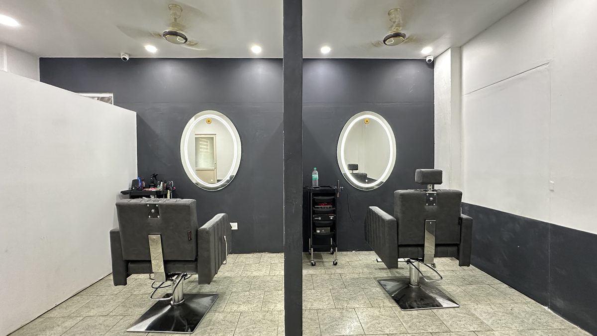 Two styling stations side by side, each with a reclining chair and a lit oval mirror on a dark grey wall.